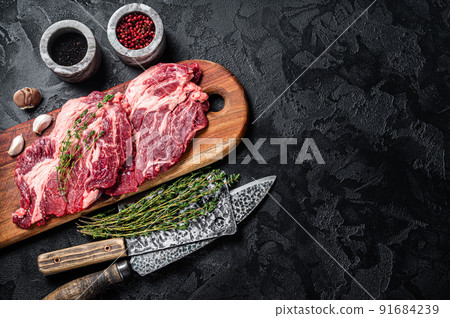Butcher marbled meat Steaks on wooden cutting board, raw beef rib-eye steaks. Black background. Top view. Copy space 91684239