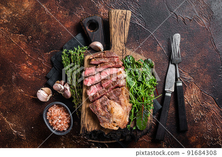 Grilled Chuck Roll beef steak with salad on wooden board. Dark background. Top view Grilled Chuck Roll beef steak with salad on wooden board. Dark background. Top view 91684308