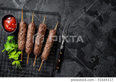 Grilled shish kebab, arabic kofta kofte kebab from mince lamb and beef meat on Skewer. Black background. Top view. Copy space Grilled shish kebab, arabic kofta kofte kebab from mince lamb and beef meat on Skewer. Black background. Top view. Copy space 91684317