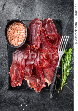 Turkish sliced pastrami (kayseri pastirma), dried beef meat with spices on marble board. Black background. Top view 91684346