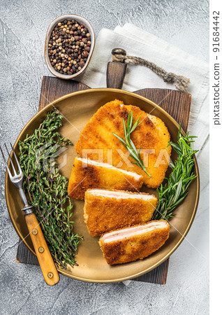 Chicken fried Cordon bleu cutlet with ham and cheese on a plate with herbs. White background. Top view 91684442