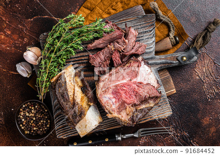 Braised veal beef short ribs on wooden cutting board with thyme. Dark background. Top view Braised veal beef short ribs on wooden cutting board with thyme. Dark background. Top view 91684452