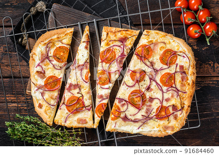 Traditional German pie Flammkuchen or tarte flambee with cream cheese, bacon, tomato and onions. Wooden background. Top view 91684460