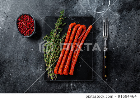 Smoked kabanos sausages with herbs on marble board. Black background. Top view 91684464