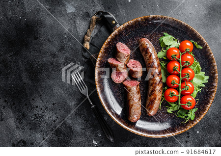 Grilled Bavarian sausage with arugula and tomato on a plate. Black background. Top view. Copy space Grilled Bavarian sausage with arugula and tomato on a plate. Black background. Top view. Copy space 91684617