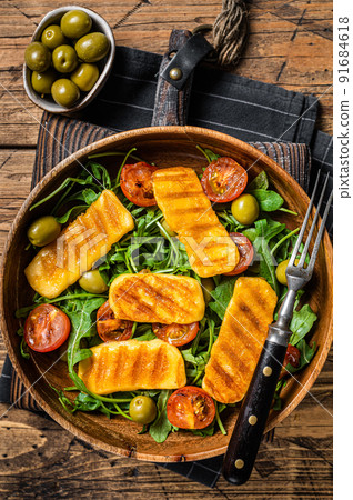 Salad with grilled Halloumi cheese, arugula, tomato and olives. Wooden background. Top view Salad with grilled Halloumi cheese, arugula, tomato and olives. Wooden background. Top view 91684618