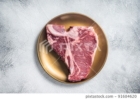 Raw T-bone porterhouse beef meat Steak on golden metalic plate. Gray background. Top view Raw T-bone porterhouse beef meat Steak on golden metalic plate. Gray background. Top view 91684620