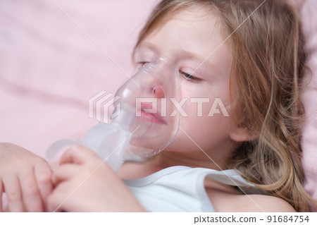 Little caucasian girl makes inhalation and breathes with special mask 91684754
