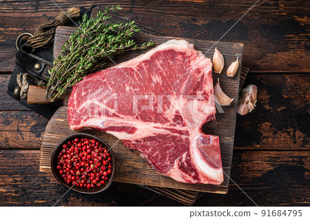 Prime T-bone beef meat steak, raw porterhouse steak on butcher board with herbs. Wooden background. Top view Prime T-bone beef meat steak, raw porterhouse steak on butcher board with herbs. Wooden background. Top view 91684795