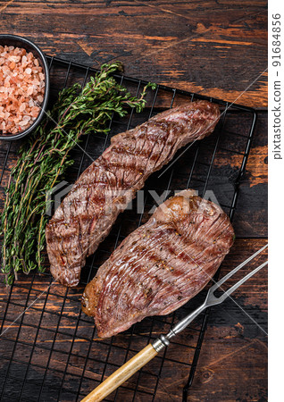 Grilled Sirloin flap or Bavette beef meat steak on a griil with herbs. Wooden background. Top view 91684856
