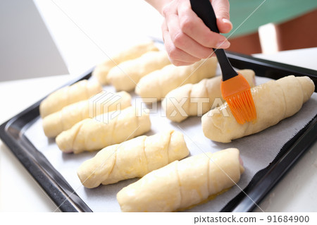 Chef brushes raw croissants with brush in yolk cooking process 91684900
