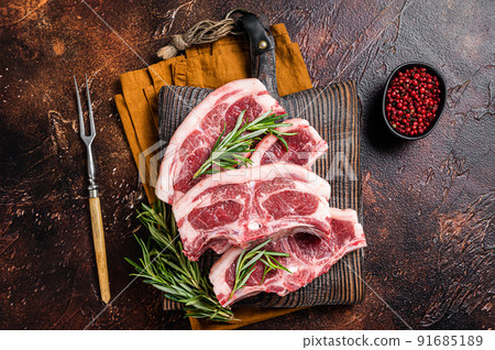 Raw fresh saddle of lamb mutton with herbs and spices on butcher board. Dark background. Top view Raw fresh saddle of lamb mutton with herbs and spices on butcher board. Dark background. Top view 91685189