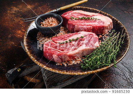Chuck eye Roll beef steaks, raw meat on a plate with thyme and herbs. Dark background. Top view Chuck eye Roll beef steaks, raw meat on a plate with thyme and herbs. Dark background. Top view 91685230