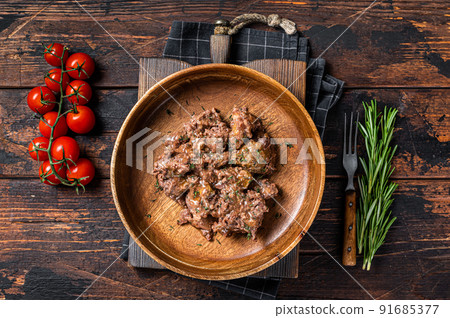 Stewed beef meat in a wooden plate. Dark Wooden background. Top view 91685377