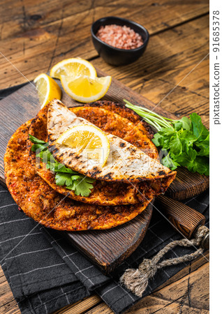 Turkish cuisine made with thin dough and minced beef meat lahmacun on wooden board with herbs. Wooden background. Top view 91685378