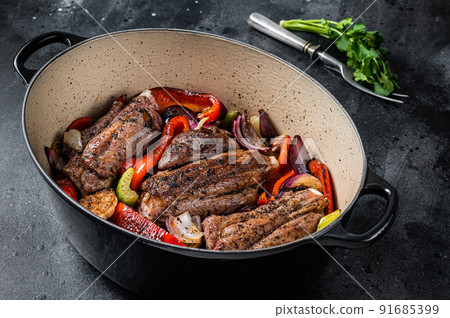 Braised slow cooked lamb shank in red wine sauce with vegetables in cooking pot. Black background. Top view Braised slow cooked lamb shank in red wine sauce with vegetables in cooking pot. Black background. Top view 91685399