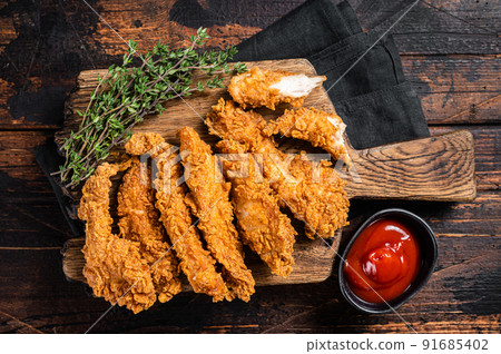 Crispy fried Breaded chicken strips, breast fillet meat with tomato ketchup on a plate. Wooden backgrund. Top view Crispy fried Breaded chicken strips, breast fillet meat with tomato ketchup on a plate. Wooden backgrund. Top view 91685402