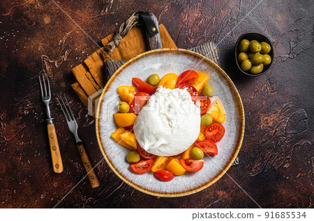 Burrata cheese and tomatoes salad served on rustic plate. Dark background. Top view Burrata cheese and tomatoes salad served on rustic plate. Dark background. Top view 91685534