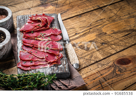 Dried Pastrami slices, beef meat with herbs on wooden board. Wooden background. Top view. Copy space Dried Pastrami slices, beef meat with herbs on wooden board. Wooden background. Top view. Copy space 91685538