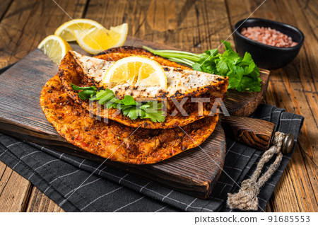 Turkish cuisine made with thin dough and minced beef meat lahmacun on wooden board with herbs. Wooden background. Top view Turkish cuisine made with thin dough and minced beef meat lahmacun on wooden board with herbs. Wooden background. Top view 91685553