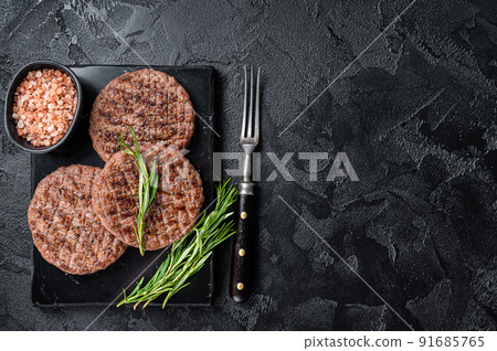 Beef burger patty cutlet for hamburger grilled on BBQ on marble board with rosemary. Black background. Top view. Copy space Beef burger patty cutlet for hamburger grilled on BBQ on marble board with rosemary. Black background. Top view. Copy space 91685765