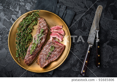 BBQ grilled Bavette Bavet beef meat steak with herbs on a plate. Black background. Top view 91685806