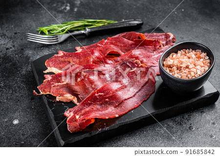 Turkish sliced pastrami (kayseri pastirma), dried beef meat with spices on marble board. Black background. Top view Turkish sliced pastrami (kayseri pastirma), dried beef meat with spices on marble board. Black background. Top view 91685842