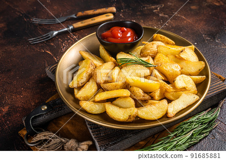 Seasoned potato wedges with rosemary and tomato sauce in a plate. Dark background. Top view 91685881