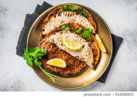 Turkish lahmacun pizza with mince meat and tomatoes on a plate with parsley and lemon. White background. Top view Turkish lahmacun pizza with mince meat and tomatoes on a plate with parsley and lemon. White background. Top view 91686005