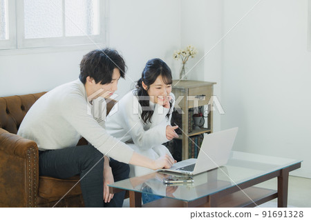 A couple looking at a computer in the living room A couple looking at a computer in the living room 91691328