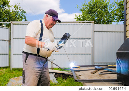 Senior gray-haired man performs welding work on metal 91691654