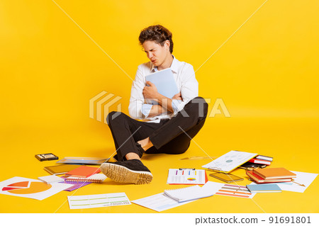 Young annoyed boy, teen in business style clothes sitting on floor and doing homework isolated over yellow background. Back to school, university Young annoyed boy, teen in business style clothes sitting on floor and doing homework isolated over yellow background. Back to school, university 91691801