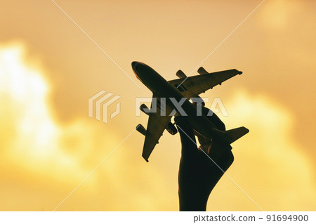 Silhouette of a hand holding a toy plane on a golden sky background Silhouette of a hand holding a toy plane on a golden sky background 91694900