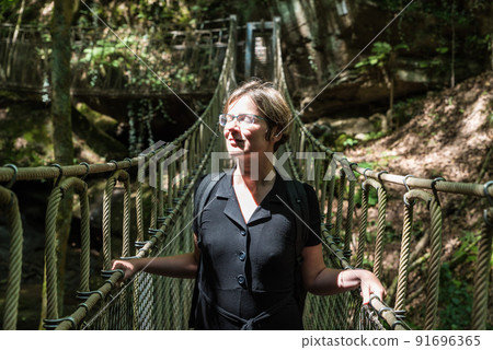 Portrait of a woman at a wooden suspension bridge over a small creek valley in the woods Portrait of a woman at a wooden suspension bridge over a small creek valley in the woods 91696365