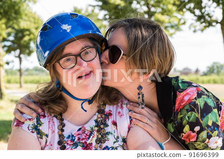 Portrait of a young white woman kissing a woman with Down Syndrome. Portrait of a young white woman kissing a woman with Down Syndrome. 91696399