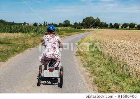 Young woman with Down syndrome driving on a tricycle through the fields at the Belgian countryside Young woman with Down syndrome driving on a tricycle through the fields at the Belgian countryside 91696406