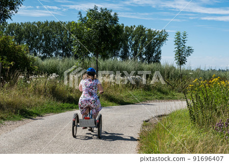 Young woman with Down syndrome driving on a tricycle through the fields at the Belgian countryside Young woman with Down syndrome driving on a tricycle through the fields at the Belgian countryside 91696407