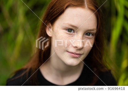 Red haired twelve year old girl with freckles posing with a nature bokeh background 91696418