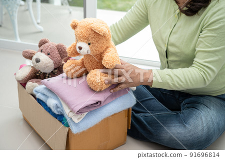 Holding clothing donation box with used clothes and doll at home to support help for poor people in the world. Holding clothing donation box with used clothes and doll at home to support help for poor people in the world. 91696814