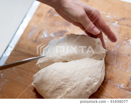 Female hands cut with a knife a kneaded dough on a wooden table. Female hands cut with a knife a kneaded dough on a wooden table. 91698077