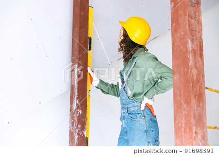 Live portrait of young woman, builder wearing helmet using different work tools at a construction site. Gender equality, job, work concept Live portrait of young woman, builder wearing helmet using different work tools at a construction site. Gender equality, job, work concept 91698391