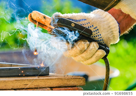 Selective focus on a hot electrode in the hand of a welder welding metal. Selective focus on a hot electrode in the hand of a welder welding metal. 91698655