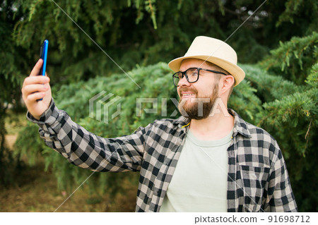 Man taking selfie portrait over tree background - Happy millennial guy enjoying summer holidays in city - Youth and technologies Man taking selfie portrait over tree background - Happy millennial guy enjoying summer holidays in city - Youth and technologies 91698712