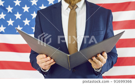 Close up of open folder in hands of unknown man in business suit on background of American flag. Close up of open folder in hands of unknown man in business suit on background of American flag. 91699366