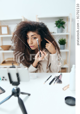 Talented tanned handsome curly Latin beauty blogger in linen shirt do smoky eyes for diy in home white interior. Copy space Mockup Banner. Influencer record video review blog using smartphone Talented tanned handsome curly Latin beauty blogger in linen shirt do smoky eyes for diy in home white interior. Copy space Mockup Banner. Influencer record video review blog using smartphone 91702110