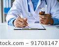 Close-up of doctor's hands writing prescription and holding bottle with pills. Healthcare, medical and pharmacy concept. 91708147