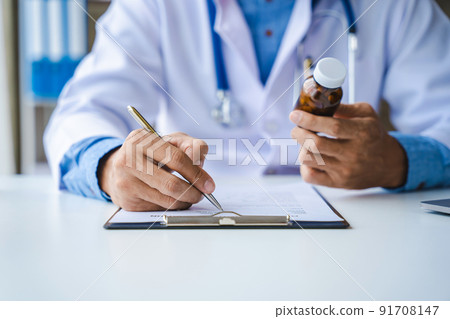 Close-up of doctor's hands writing prescription and holding bottle with pills. Healthcare, medical and pharmacy concept. Close-up of doctor's hands writing prescription and holding bottle with pills. Healthcare, medical and pharmacy concept. 91708147