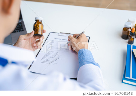 Close-up of doctor's hands writing prescription and holding bottle with pills. Healthcare, medical and pharmacy concept. 91708148