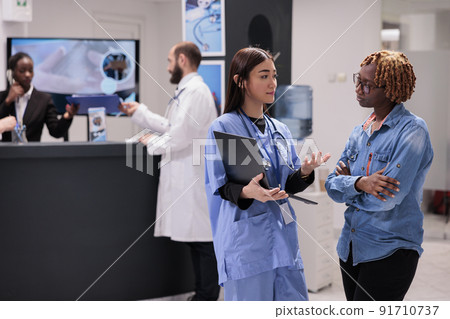 Asian nurse showing healthcare diagnosis to patient in hospital reception lobby, explaining medical results on laptop. Diverse women talking about medicine treatment and recovery in waiting area. Asian nurse showing healthcare diagnosis to patient in hospital reception lobby, explaining medical results on laptop. Diverse women talking about medicine treatment and recovery in waiting area. 91710737