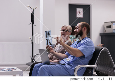 Medical assistant showing x ray to elderly patient, sitting in hospital reception lobby. Nurse explaining radiography scan results to woman with disease, talking about treatment and diagnosis. Medical assistant showing x ray to elderly patient, sitting in hospital reception lobby. Nurse explaining radiography scan results to woman with disease, talking about treatment and diagnosis. 91710911